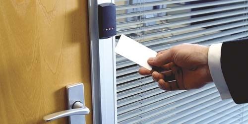 Hand håller ett passerkort framför en elektronisk dörrläsare