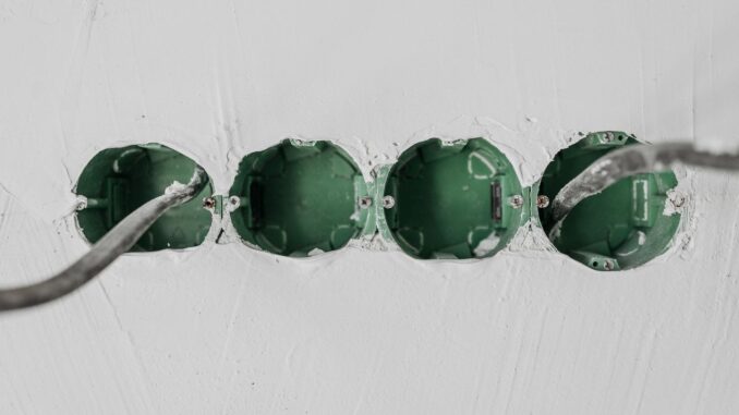 Fyra infällda gröna apparatdosor med kablar i en vit vägg